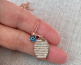 Può includere: Collana in oro rosa con un ciondolo ovale con calligrafia araba e un ciondolo con occhio blu.