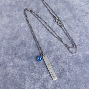 May include: Silver chain necklace with a blue evil eye charm and a silver pendant with Arabic calligraphy.