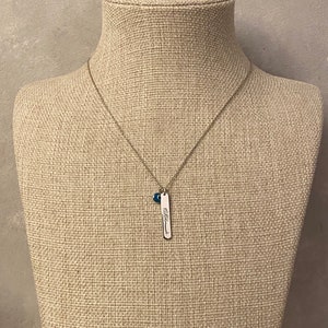 May include: A silver necklace with a small blue bead charm and a silver pendant with the word "blessed" engraved on it.