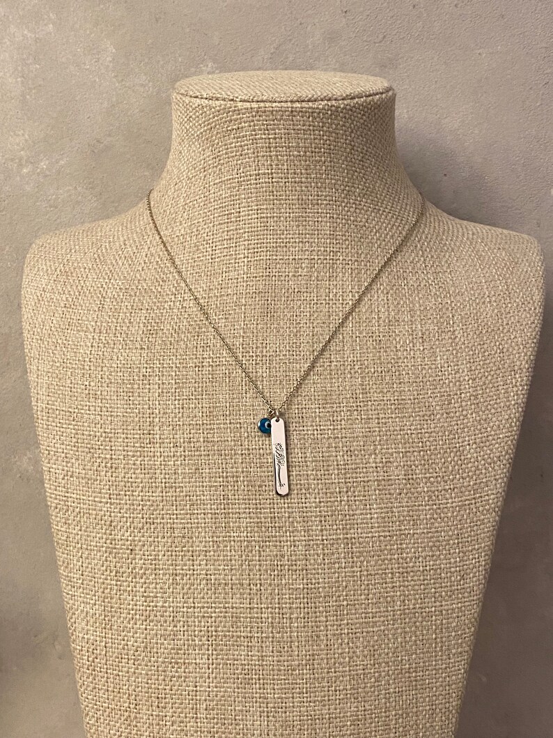 May include: A silver necklace with a small blue bead charm and a silver pendant with the word "blessed" engraved on it.