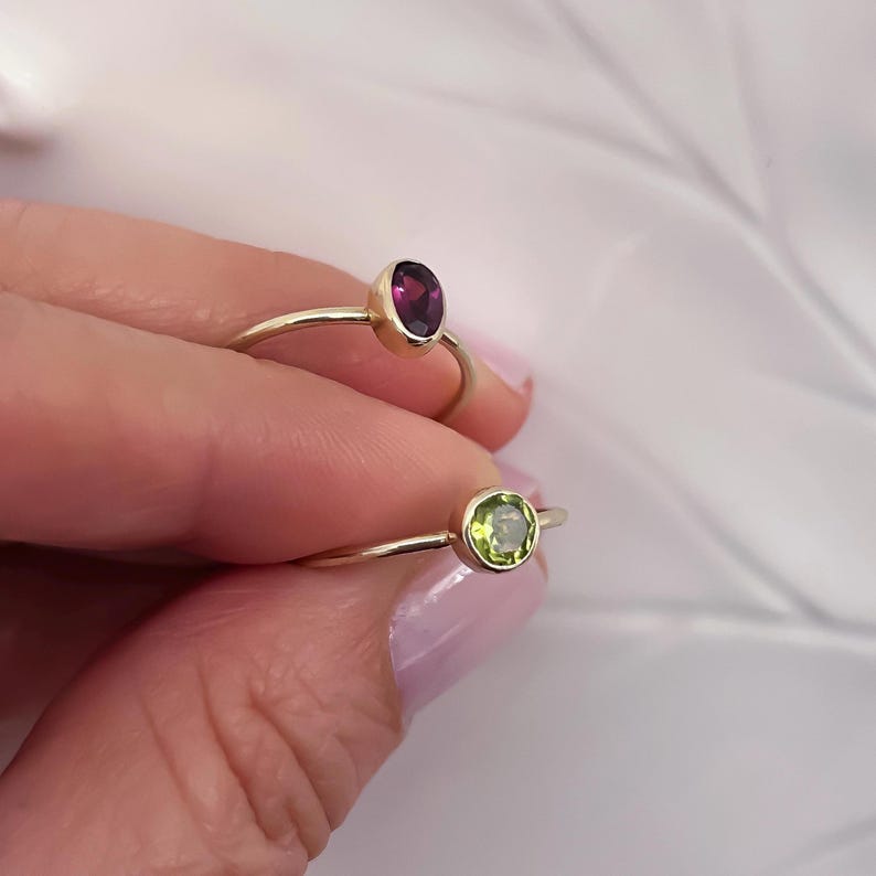 Pu&ograve; includere: Due anelli d'oro con pietre preziose. L'anello superiore ha una pietra ovale di colore viola. L'anello inferiore ha una pietra rotonda di colore verde.