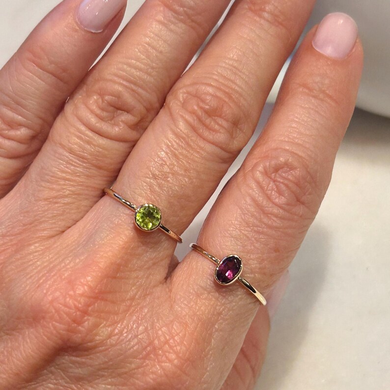 Pu&ograve; includere: Due delicati anelli d'oro con piccole pietre preziose. L'anello a sinistra ha una pietra preziosa verde, mentre l'anello a destra ha una pietra preziosa viola.