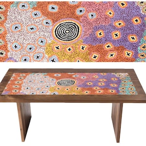 Puede incluir: Mesa rectangular de madera con un diseño abstracto y colorido en la superficie. El diseño presenta una espiral central rodeada de puntos y formas en naranja, morado, amarillo y azul. La mesa tiene un marco y patas de madera marrón oscuro.