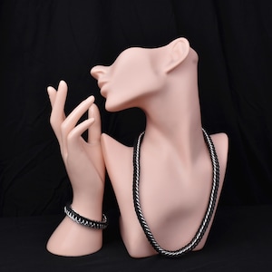 May include: A silver and black chain necklace and bracelet. The necklace is on a mannequin bust and the bracelet is on a mannequin hand.