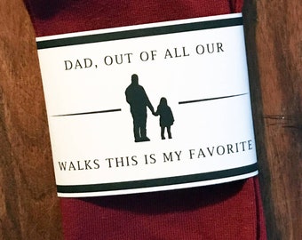 May include: Red socks with a white label that says "Dad, out of all our walks this is my favorite" with a silhouette of a father and child holding hands.