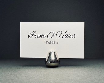 May include: White card with black text reading "Irene O'Hara" and "Table 4" in a silver card holder.