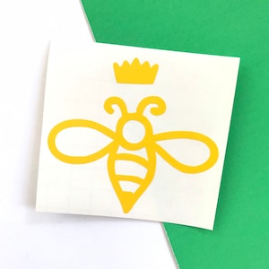 May include: A yellow bee with a crown on its head. The bee is outlined in white and has a striped body.