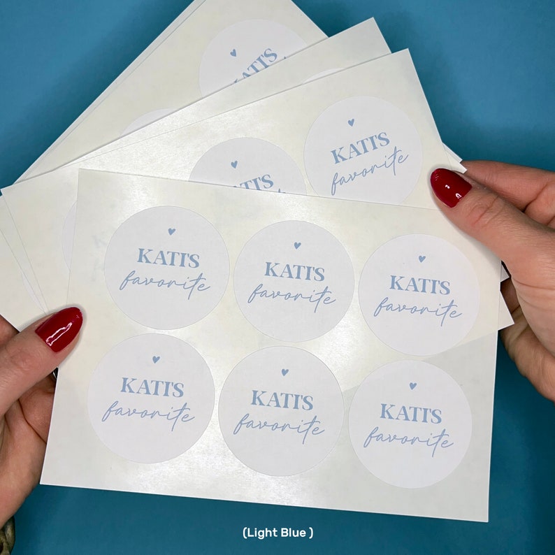 May include: A sheet of white sticker paper with eight round stickers. Each sticker has a light blue circle with the text "KATIS favorite" in a handwritten font.