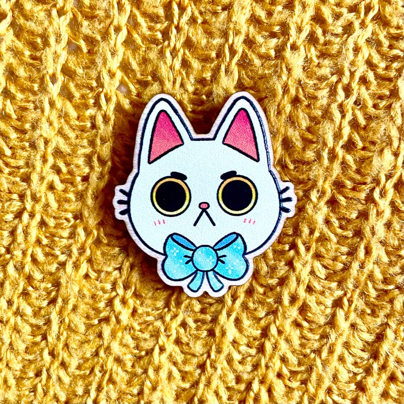 May include: White wooden cat pin with blue bow tie. The cat has large eyes and a cute expression.