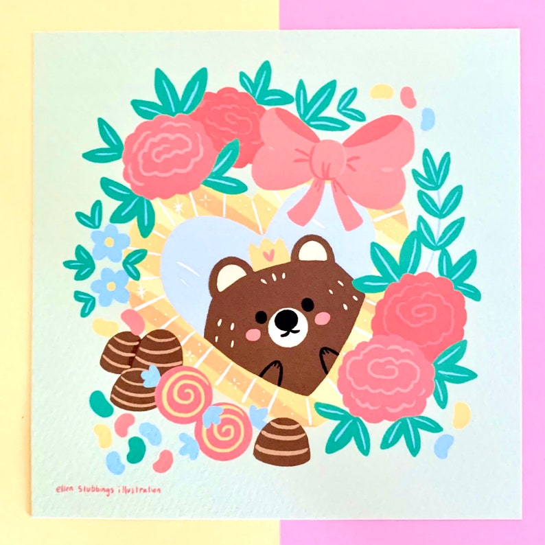 May include: A brown bear wearing a crown sits inside a heart-shaped frame surrounded by pink and blue flowers, candy, and a pink bow. The background is a light green.
