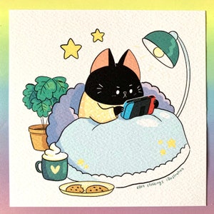 Könnte beinhalten: Eine schwarze Katze, die ein gelbes und weißes Hemd mit Muster trägt, liegt im Bett und spielt ein Videospiel. Die Katze liegt unter einer blauen Decke mit weißen Wolken. Es gibt ein Nachtlicht, eine Topfpflanze, eine Tasse heiße Schokolade und zwei Kekse auf einem Teller.