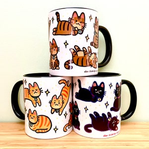 May include: Three white ceramic mugs with black handles. Each mug features a different pattern of cartoon cats with stars. The mugs are stacked on top of each other. The text "ellen stubbings illustra" is printed on the bottom of each mug.