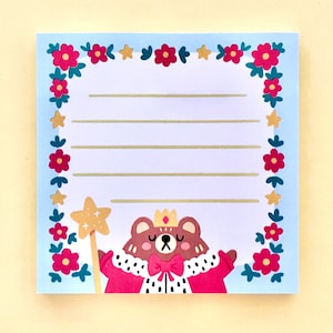 May include: A blue notepad with a floral border and a cartoon bear wearing a crown and a red robe. The bear is holding a gold star wand.