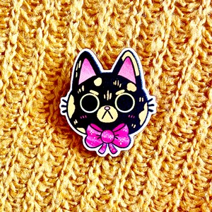 May include: A black and white cat with pink ears and a pink bow tie. The cat is cartoon-style and has a surprised expression.