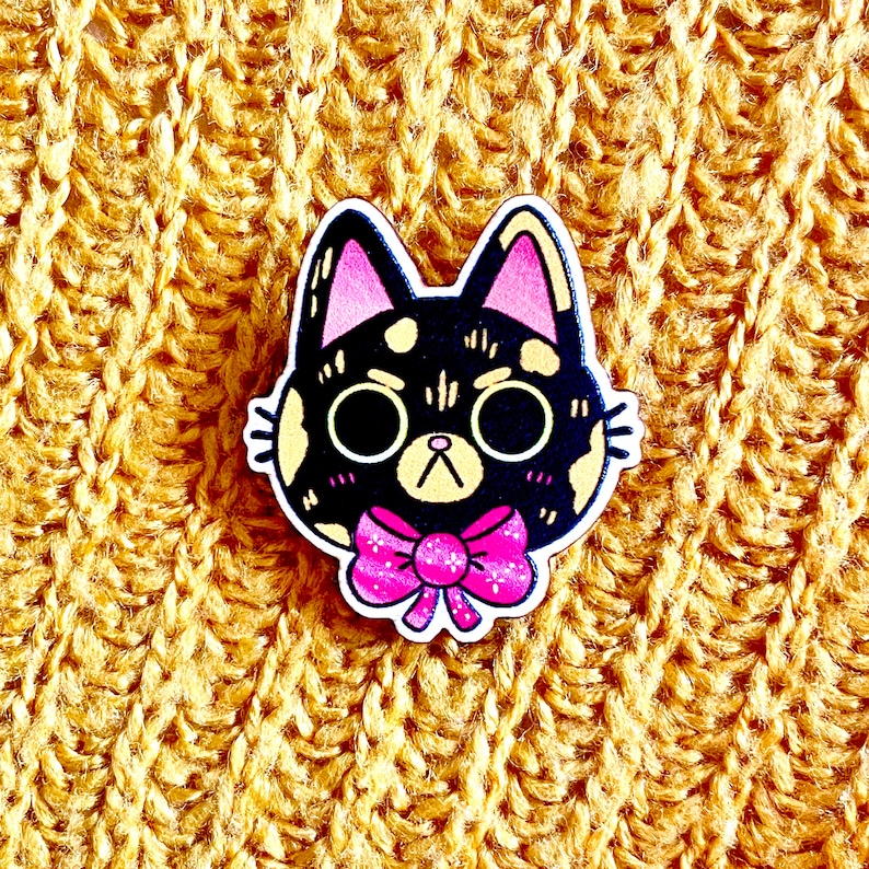 May include: A black and white cat with pink ears and a pink bow tie. The cat is cartoon-style and has a surprised expression.