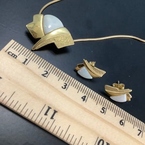Op de afbeelding: Een gouden ketting en oorbellen set met een witte opaal steen. De ketting heeft een geometrisch ontwerp en de oorbellen zijn eenvoudige studs.