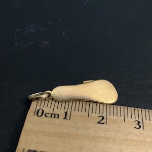 K&ouml;nnte beinhalten: Ein goldfarbener Metallanh&auml;nger in Fu&szlig;form, der an einem Holzlineal liegt. Der Anh&auml;nger misst etwa 2,2 Zentimeter in der L&auml;nge, gemessen von der Spitze des Verbindungsrings bis zur Ferse, wie auf der sichtbaren metrischen Skala zu sehen.