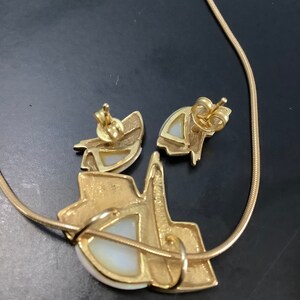 Op de afbeelding: Een gouden ketting en bijpassende oorbellen met een witte opaal in het midden van elk stuk. De ketting is een simpele ketting en de oorbellen zijn van het oorbel-type.