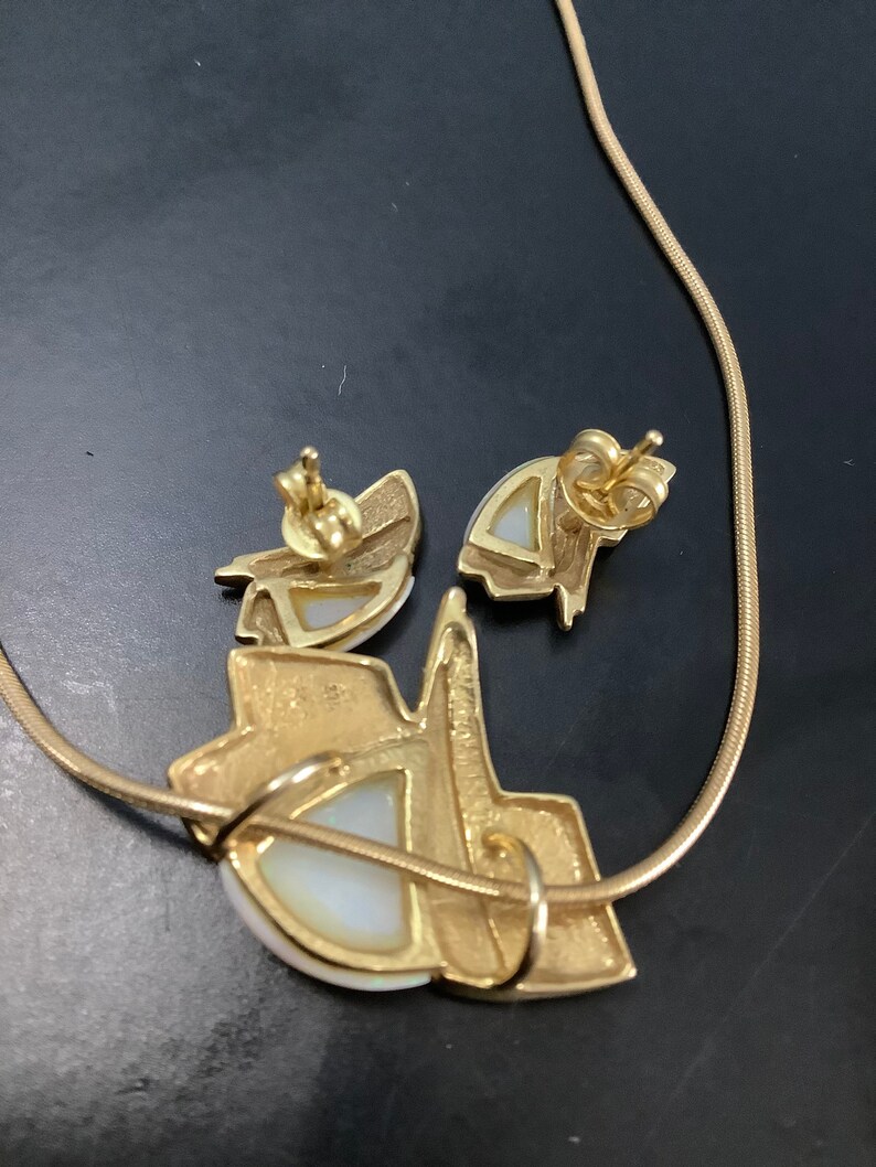 Op de afbeelding: Een gouden ketting en bijpassende oorbellen met een witte opaal in het midden van elk stuk. De ketting is een simpele ketting en de oorbellen zijn van het oorbel-type.