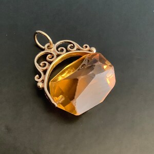 May include: A gold pendant with a large, faceted, amber-colored gemstone. The pendant has a decorative, ornate bail.