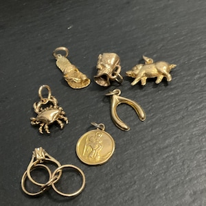 Peut inclure: Une collection de bijoux dorés comprenant une breloque tong, un petit seau, une figurine de cochon, une breloque crabe, un os à souhait, un pendentif circulaire représentant une silhouette et deux anneaux entrelacés avec un sertissage.