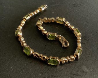 May include: A gold bracelet with a delicate, ornate design features oval-shaped green gemstones. The bracelet has a clasp closure.