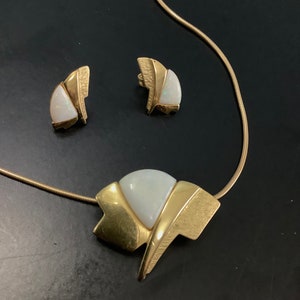 Op de afbeelding: Een gouden ketting en oorbellen set met een witte opaal steen in een geometrisch ontwerp.
