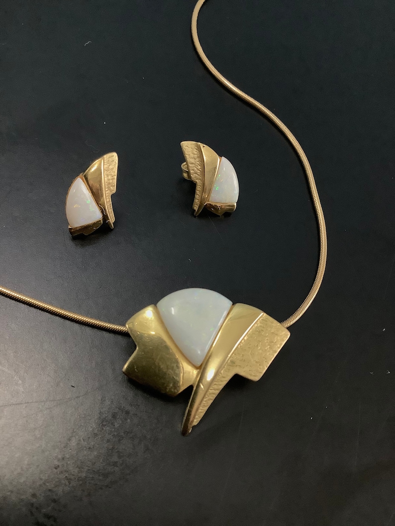 Op de afbeelding: Een gouden ketting en oorbellen set met een witte opaal steen in een geometrisch ontwerp.