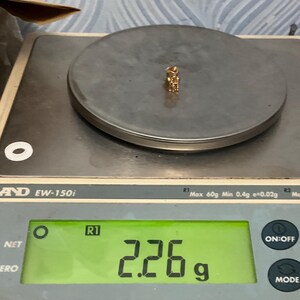 K&ouml;nnte beinhalten: Ein kleiner goldfarbener Anh&auml;nger liegt auf der runden Plattform einer digitalen Waage. Das Display der Waage zeigt ein Gewicht von 2,26 Gramm an. Der Anh&auml;nger hat eine metallische Oberfl&auml;che und ein kompaktes, filigranes Design.
