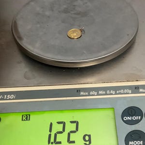 K&ouml;nnte beinhalten: Ein kleiner, runder, goldfarbener Anh&auml;nger mit gepr&auml;gtem Design, der auf einer digitalen Waage liegt. Das Display der Waage zeigt ein Gewicht von 1,22 Gramm an, wobei eine maximale Kapazit&auml;t von 60 Gramm und ein Minimum von 0,4 Gramm sichtbar sind.