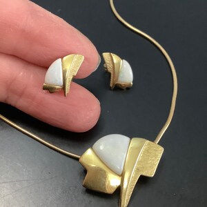 Op de afbeelding: Een gouden ketting en oorbellenset met een witte opaalsteen in een geometrisch ontwerp.