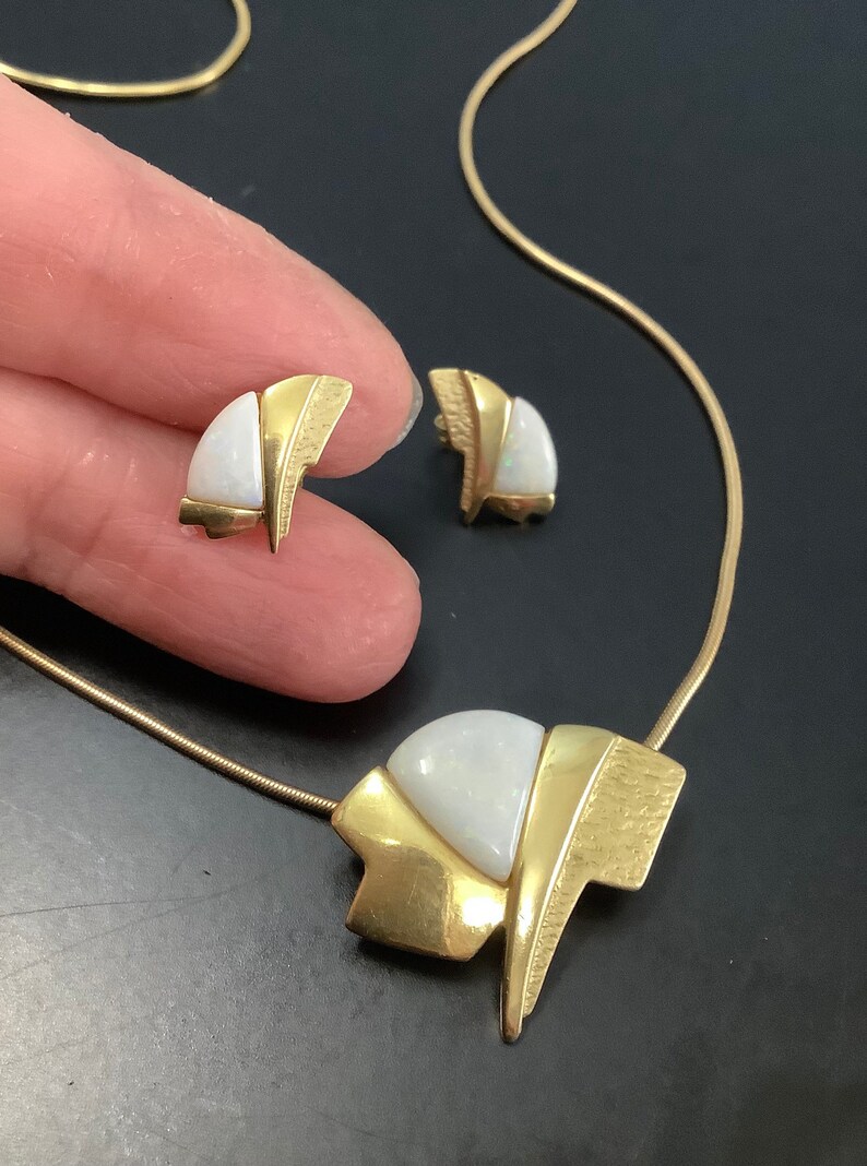 Op de afbeelding: Een gouden ketting en oorbellenset met een witte opaalsteen in een geometrisch ontwerp.