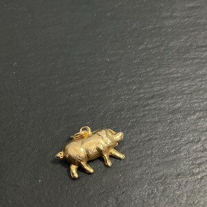 K&ouml;nnte beinhalten: Ein kleiner, dreidimensionaler goldfarbener Anh&auml;nger in Form eines Schweins mit polierter metallischer Oberfl&auml;che und einem kleinen runden Biegering an der Oberseite zur Befestigung. Das Schwein ist in stehender Position mit vier Beinen dargestellt.