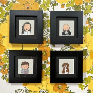 May include: Four black picture frames with white mats, each containing a hand-drawn illustration. The top left frame shows a woman with short brown hair, the top right frame shows a man with a beard, the bottom left frame shows a person with short brown hair, and the bottom right frame shows a brown and white dog.