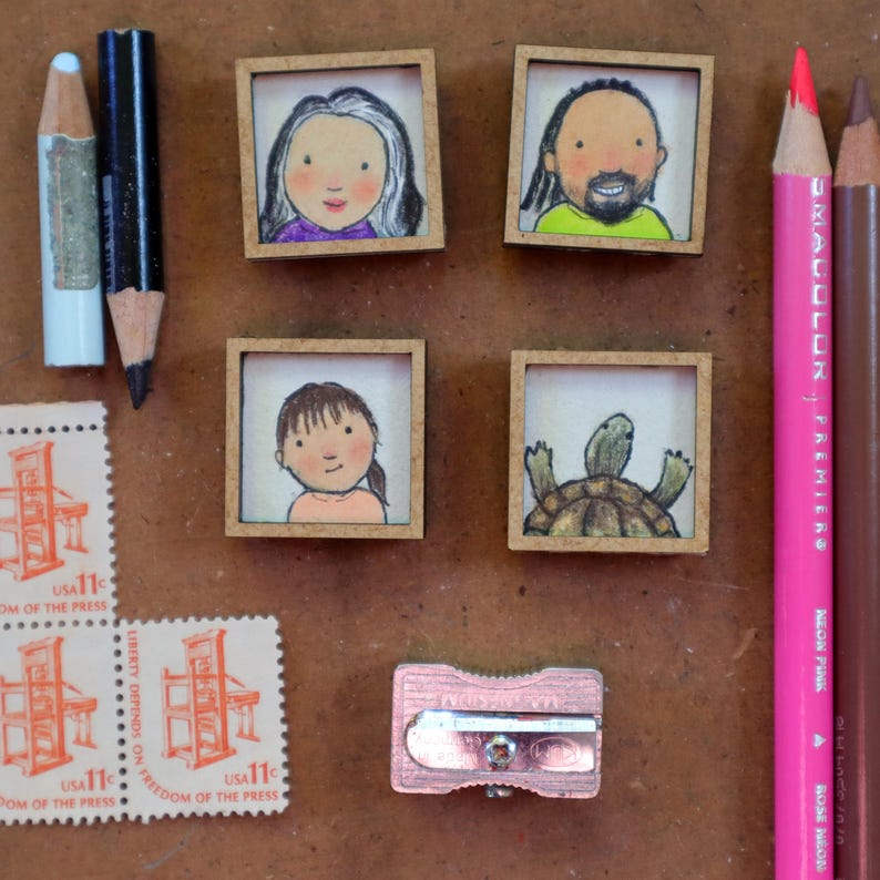 May include: A collection of miniature framed illustrations, including portraits and a turtle, alongside colored pencils, stamps, and a pencil sharpener. The stamps read "USA 11" and "FREEDOM OF THE PRESS". The pencils are pink, brown, and blue.