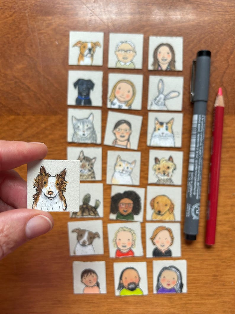May include: A collection of small, square watercolor paintings featuring portraits of people and pets. A hand holds one painting of a dog. A gray pen and a red pencil are also in the image.
