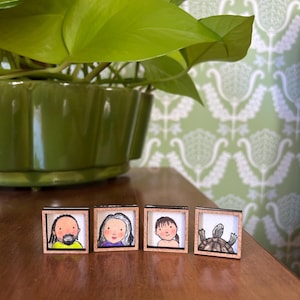 May include: Four small, square framed illustrations. The illustrations depict a person with a beard, a person with gray hair, a person with brown hair, and a turtle. The frames are made of wood.