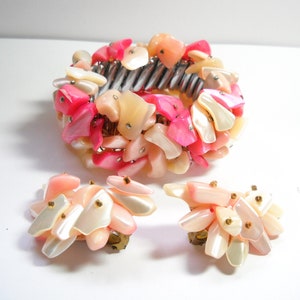 K&ouml;nnte beinhalten: Ein Set aus rosa und wei&szlig;en Muschel-Schmuck, bestehend aus einem Armband und einem Paar Ohrringen. Das Armband besteht aus einem Metallband mit einer Ansammlung von rosa und wei&szlig;en Muschelteilen. Die Ohrringe sind ebenfalls aus rosa und wei&szlig;en Muschelteilen gefertigt und haben einen Clipverschluss.