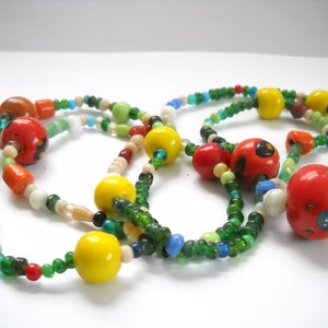 Op de afbeelding: Een kleurrijke kralenketting met groene, rode, gele en witte kralen. De ketting heeft grotere, ronde kralen met beschilderde ontwerpen.