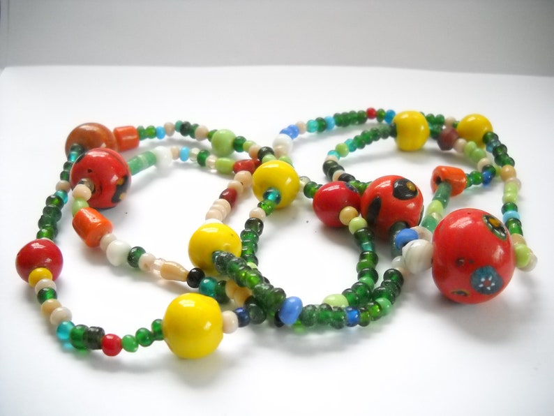 Op de afbeelding: Een kleurrijke kralenketting met groene, rode, gele en witte kralen. De ketting heeft grotere, ronde kralen met beschilderde ontwerpen.