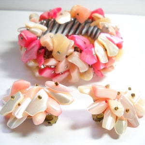 K&ouml;nnte beinhalten: Ein Set aus rosa und wei&szlig;en Muschel-Schmuck, bestehend aus einem Armband und einem Paar Ohrringen. Der Schmuck ist aus schillernden Muschelteilen gefertigt und hat goldene Akzente.