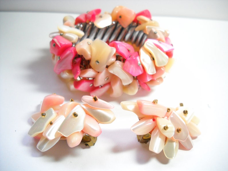 K&ouml;nnte beinhalten: Ein Set aus rosa und wei&szlig;en Muschel-Schmuck, bestehend aus einem Armband und einem Paar Ohrringen. Der Schmuck ist aus schillernden Muschelteilen gefertigt und hat goldene Akzente.