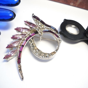 May include: A silver tone brooch with a swirling design set with clear and pink rhinestones.