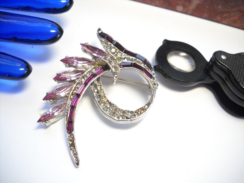 May include: A silver tone brooch with a swirling design set with clear and pink rhinestones.
