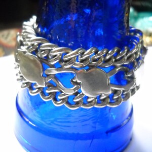 May include: A silver chain bracelet with a unique design featuring interlocking links and heart-shaped charms. The bracelet is displayed on a blue background.
