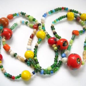 Op de afbeelding: Een kleurrijke kralenketting met rode, gele, groene en witte kralen. De ketting is gemaakt van glazen kralen en heeft verschillende vormen en maten.