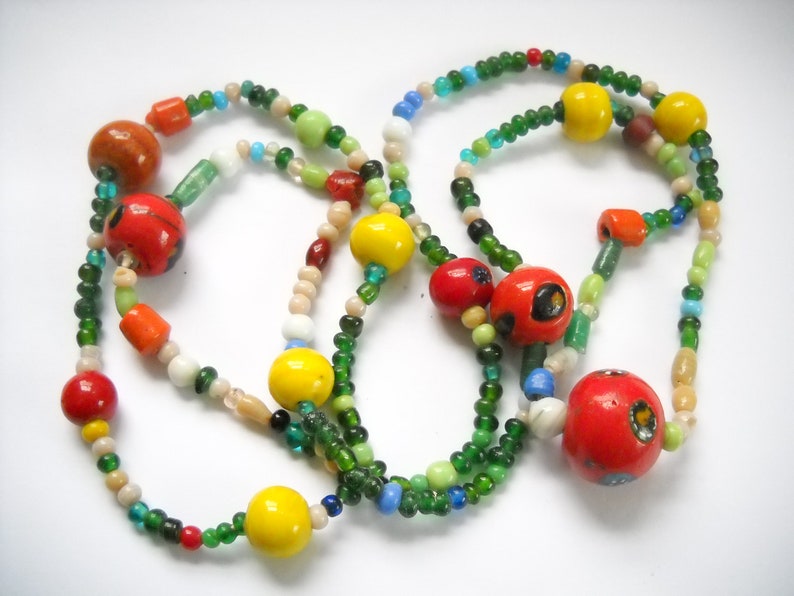 Op de afbeelding: Een kleurrijke kralenketting met rode, gele, groene en witte kralen. De ketting is gemaakt van glazen kralen en heeft verschillende vormen en maten.