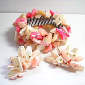 K&ouml;nnte beinhalten: Ein Armband und Ohrringe Set aus rosa und wei&szlig;en Muscheln. Das Armband besteht aus einem Metallband, an dem rosa und wei&szlig;e Muschelteile befestigt sind. Die Ohrringe bestehen ebenfalls aus rosa und wei&szlig;en Muschelteilen.