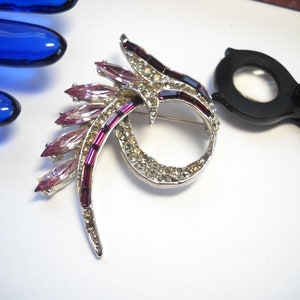 May include: A silver tone brooch with a swirl design set with clear and pink rhinestones.