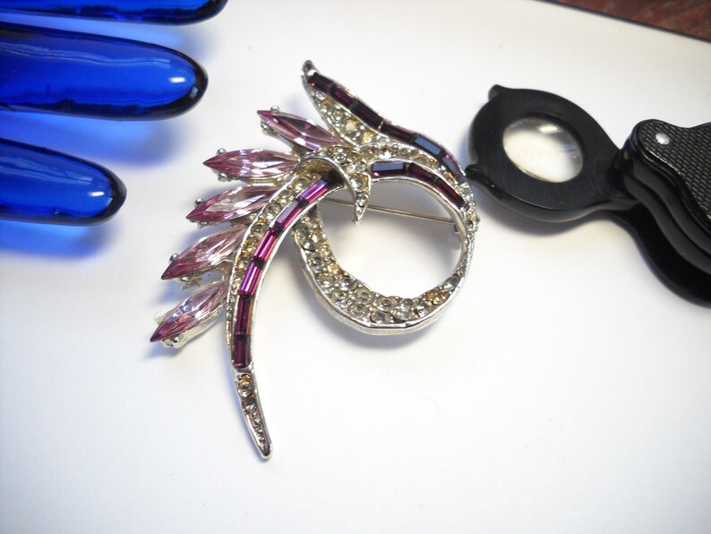 May include: A silver tone brooch with a swirl design set with clear and pink rhinestones.